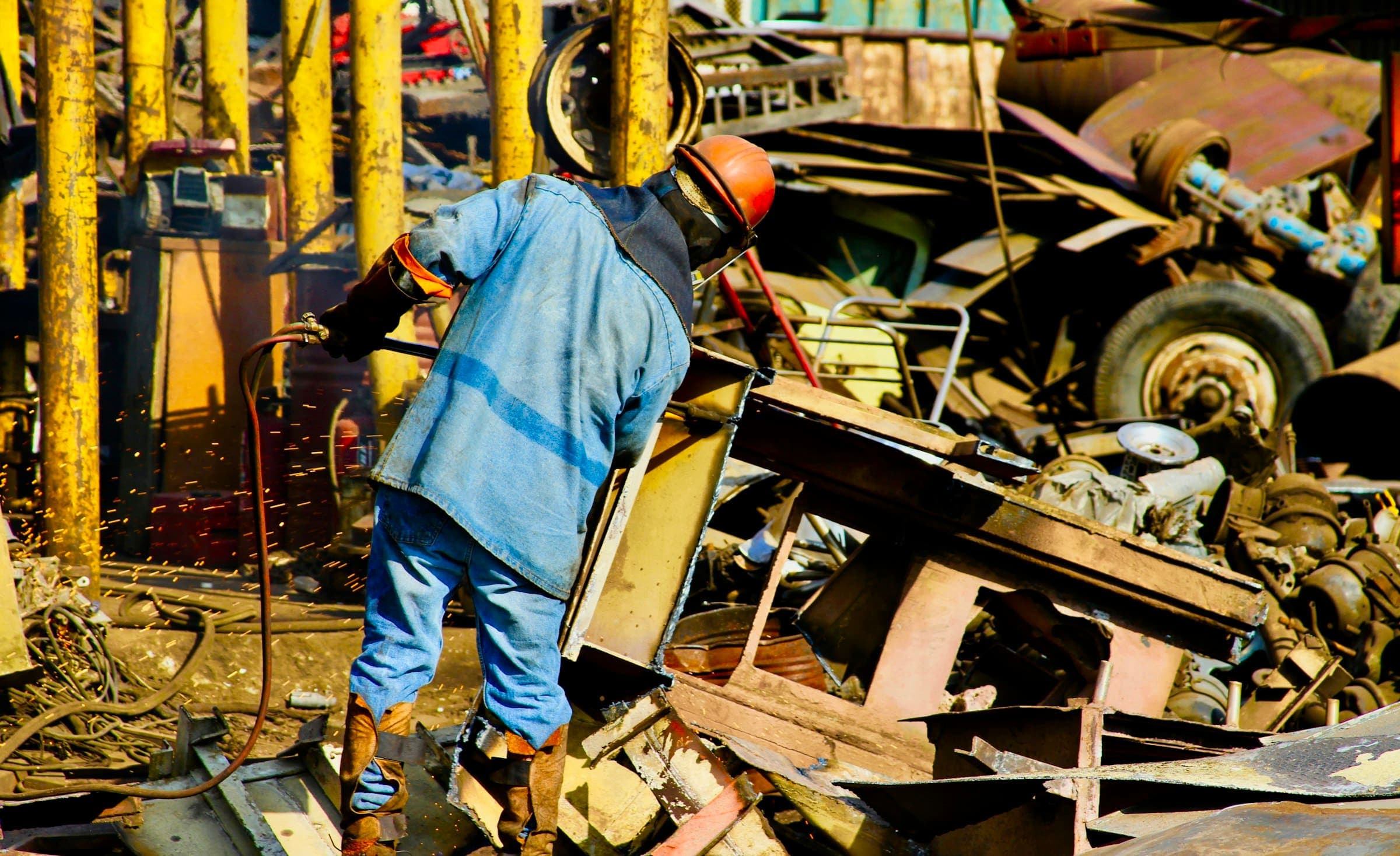 Cutting up scrap metal with a torch A worker in a hard hat cutting up scrap metal with a gas torch as sparks fly
