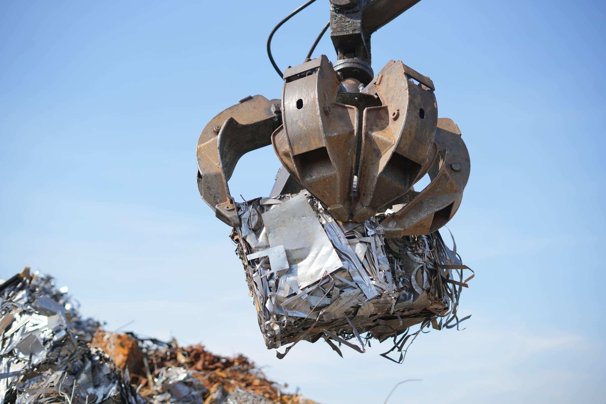 A grapple holding a crushed bale of scrap metal against a blue sky A grapple holding a crushed bale of scrap metal against a blue sky